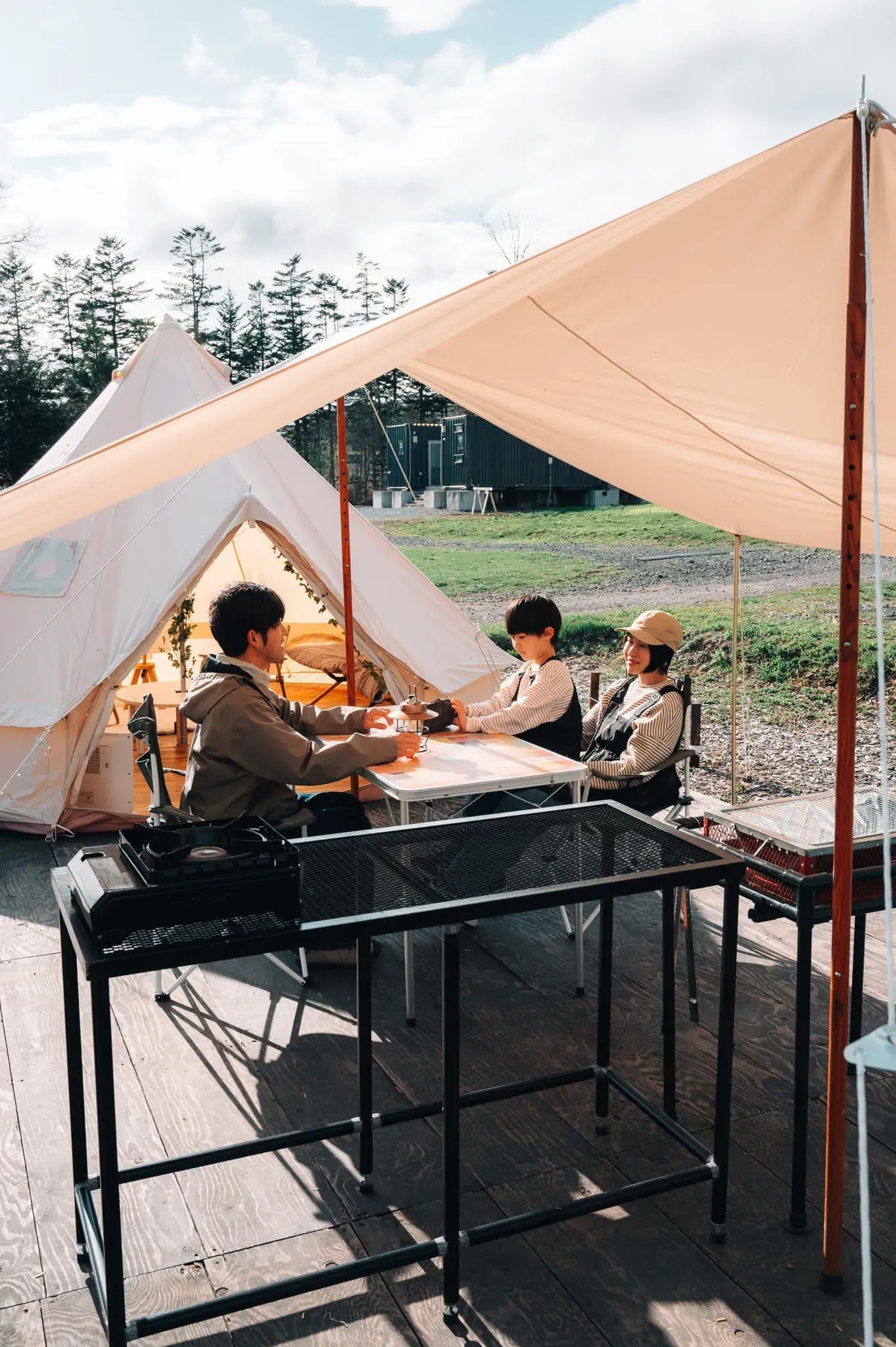 ベルテントの前で家族がテーブルを囲むキャンプ風景